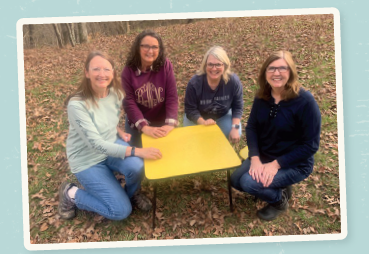 4 women kneeling around a yellow table