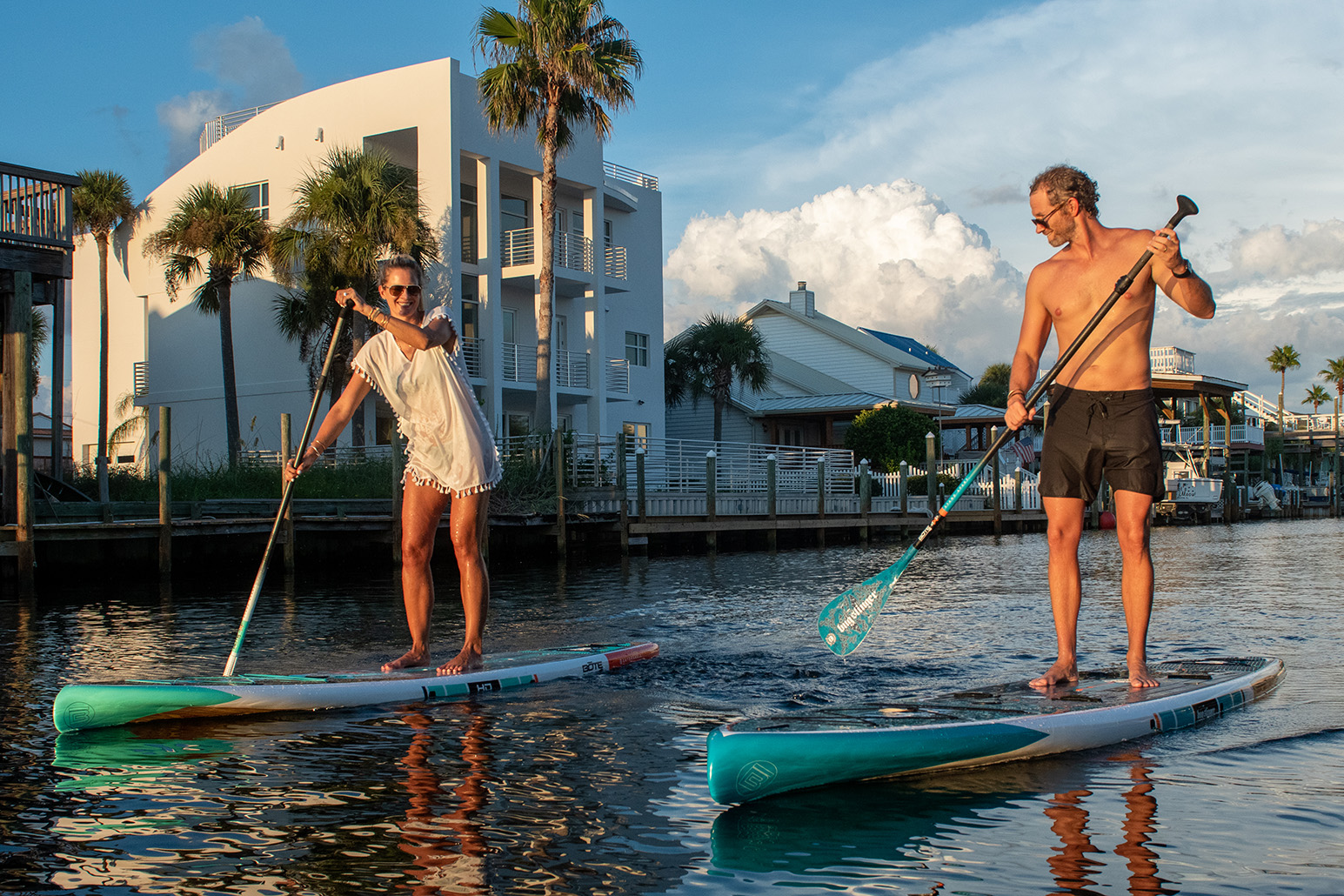 Corey and Magda Cooper standing on BOTE boards in the water as the sun sets.