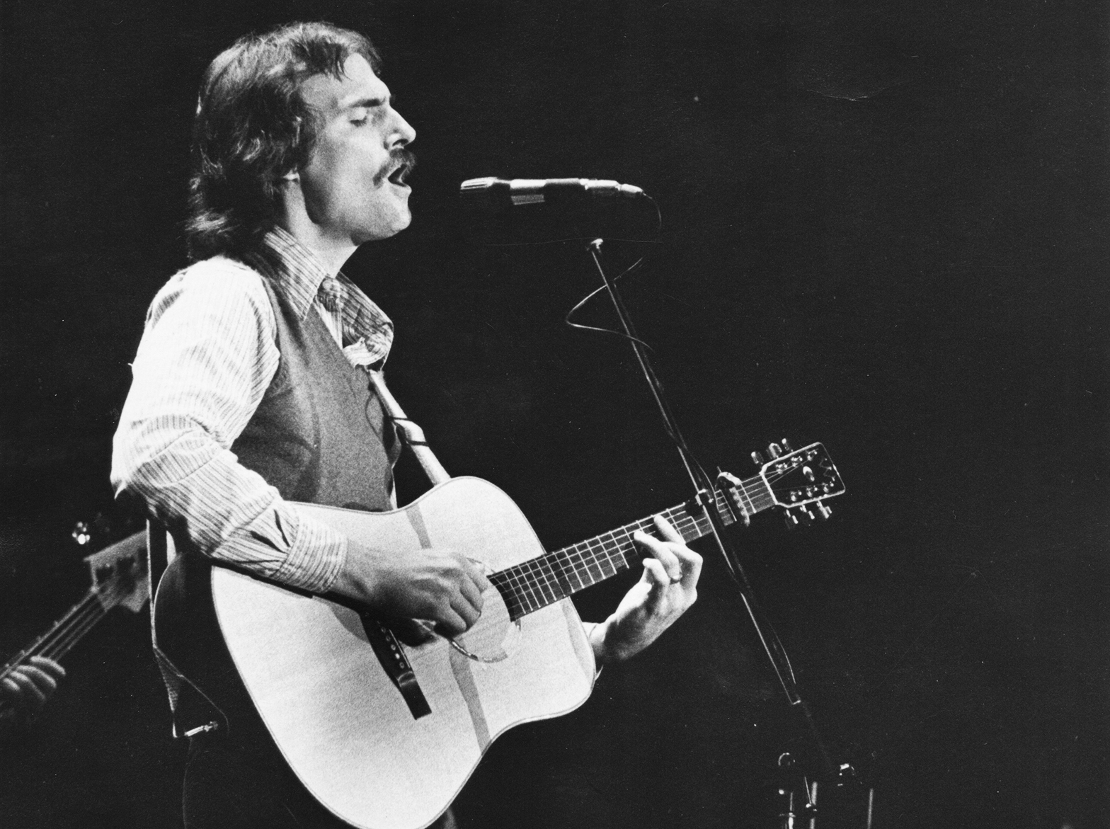 James Taylor strumming his guitar on stage while singing into microphone