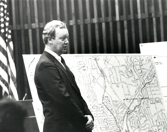 Man in a suit standing in a court room in front of a map