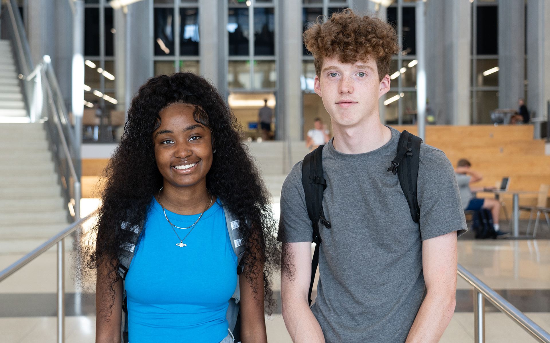 black female and white male student standing side by side in a library with their backpacks on