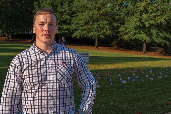 young veteran stands in front of lawn decorated with American flags