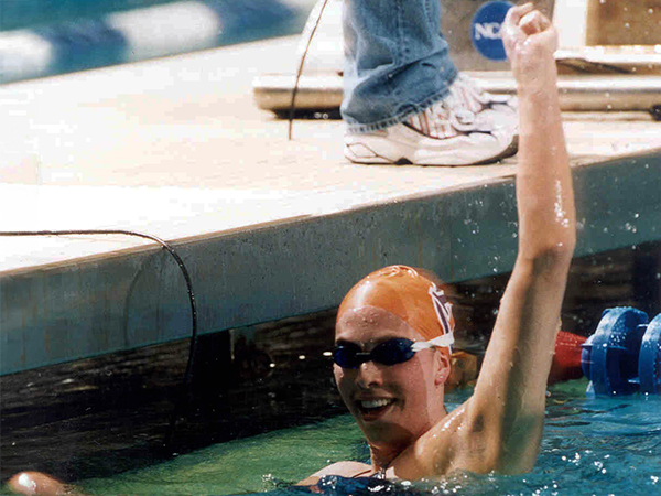 Female swimmer hanging on the the edge of a pool celebrating finishing a lap with one arm raised