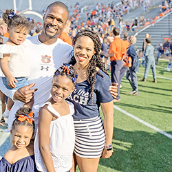 young black family dressed in Auburn attire posing for a photo on a football field