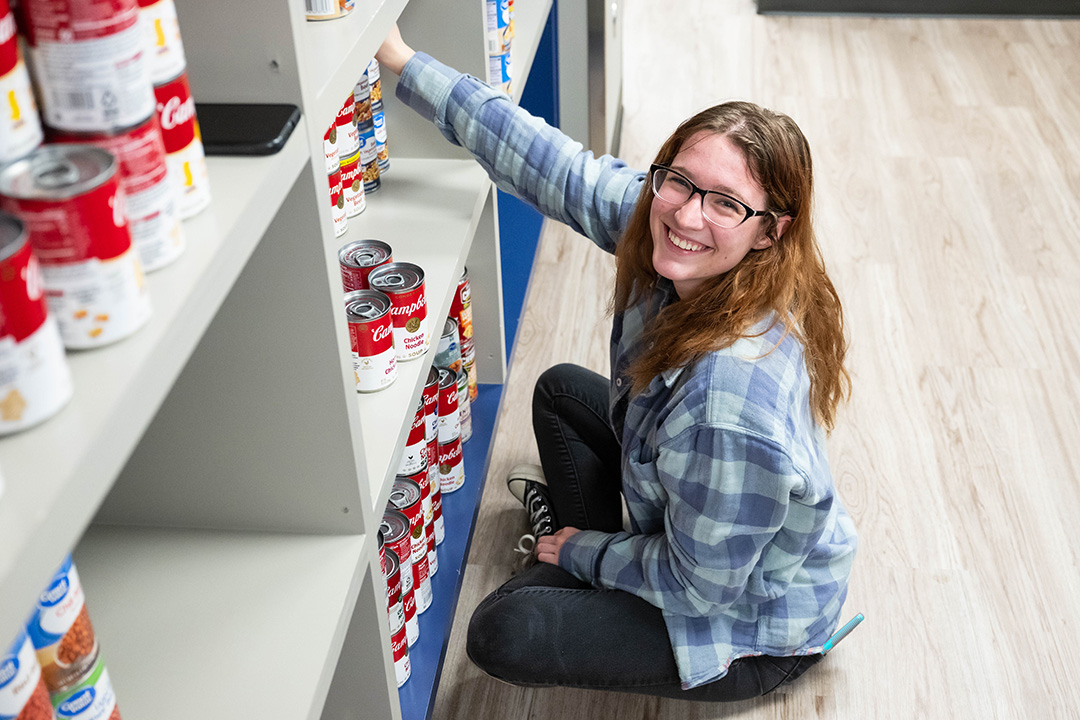 Girl stocking shelves with soup cans at campus pantry